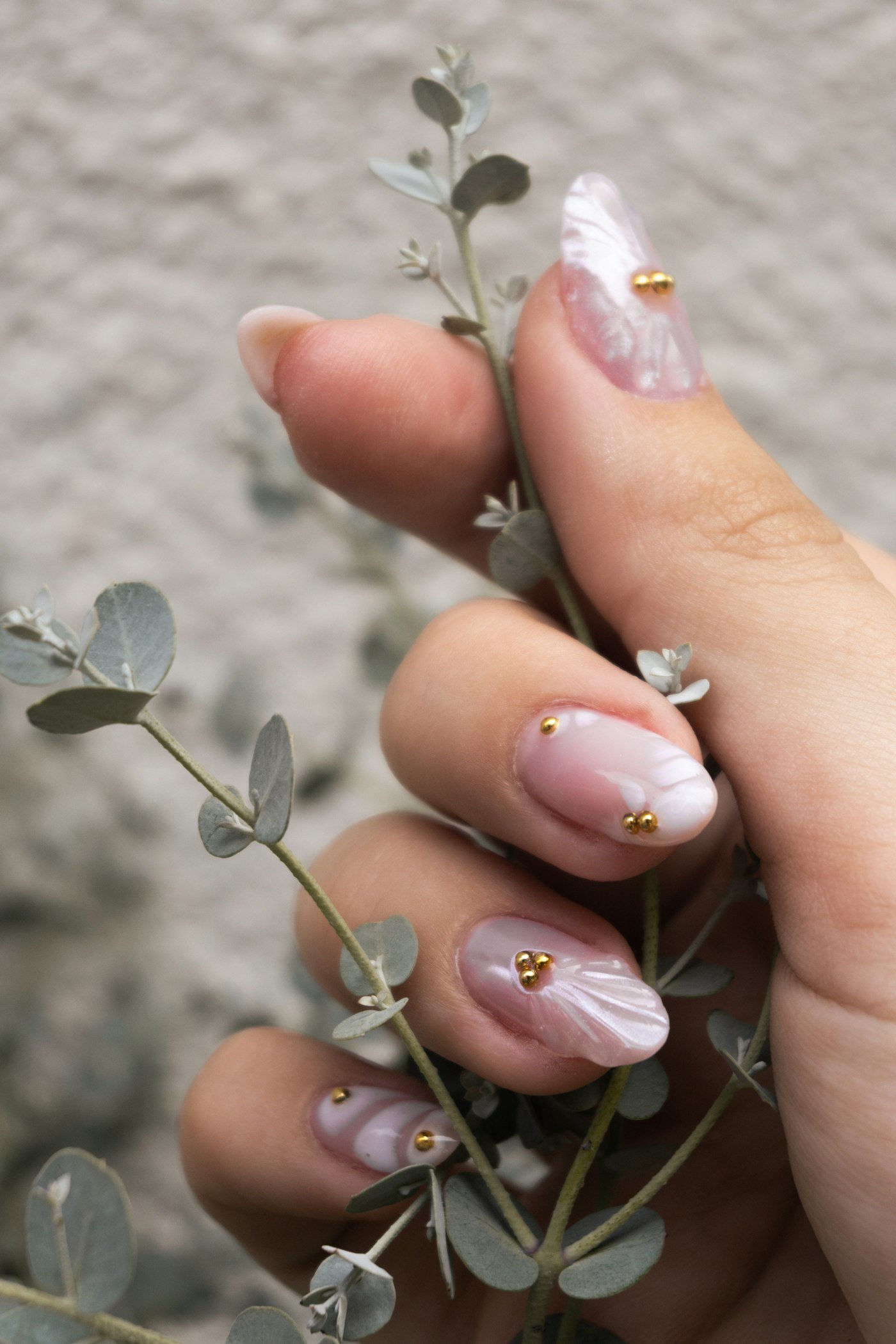 Hand with delicate floral nail art holding a sprig of eucalyptus