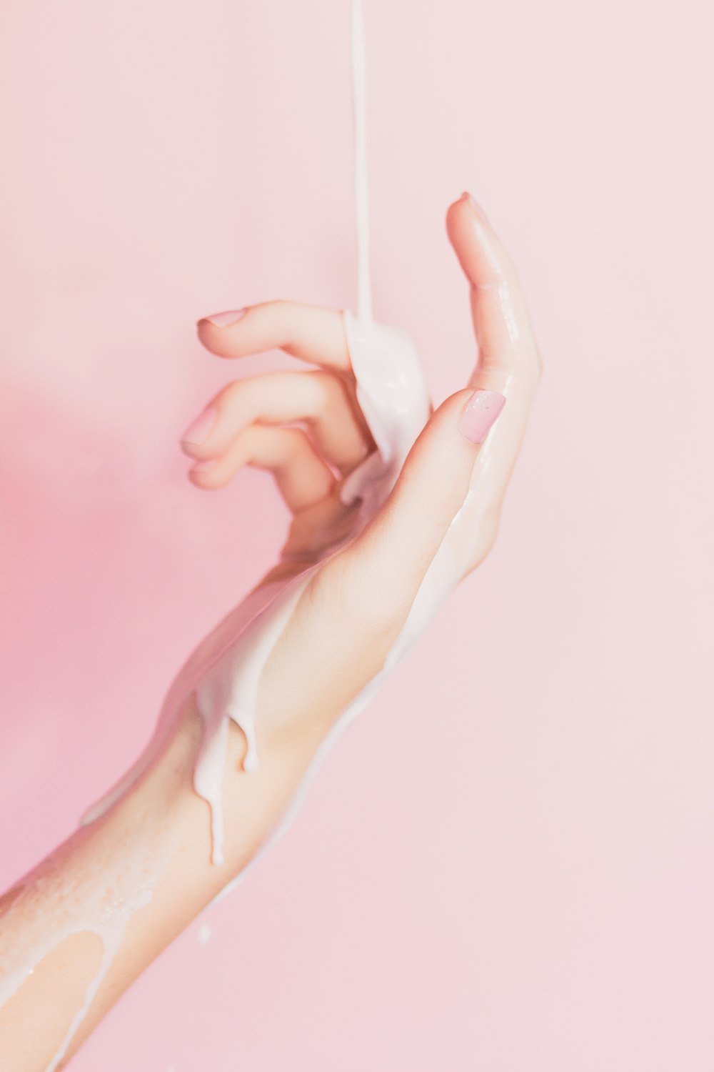 Silky lotion poured over a hand on a soft pink background