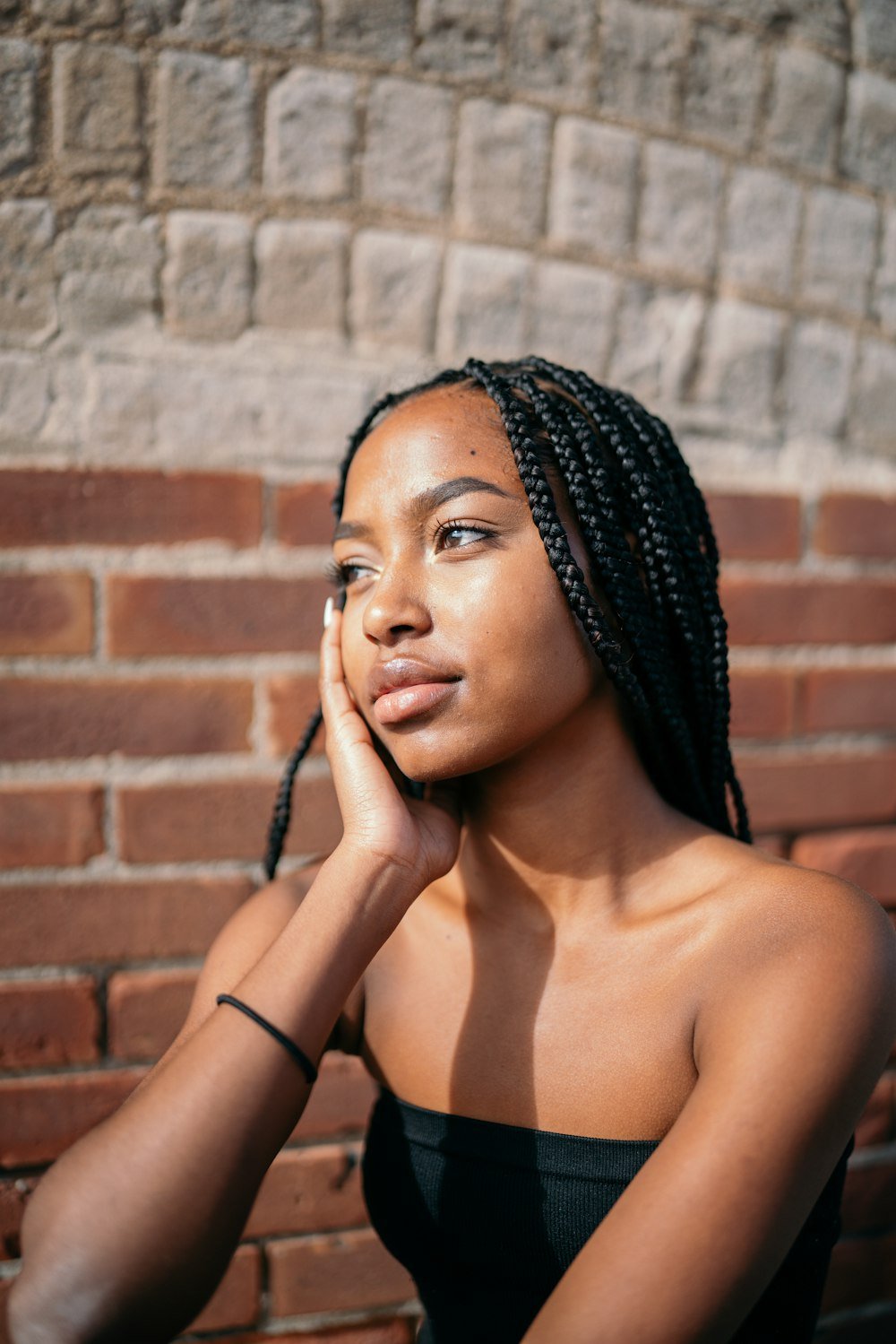 Woman with braids against a brick wall