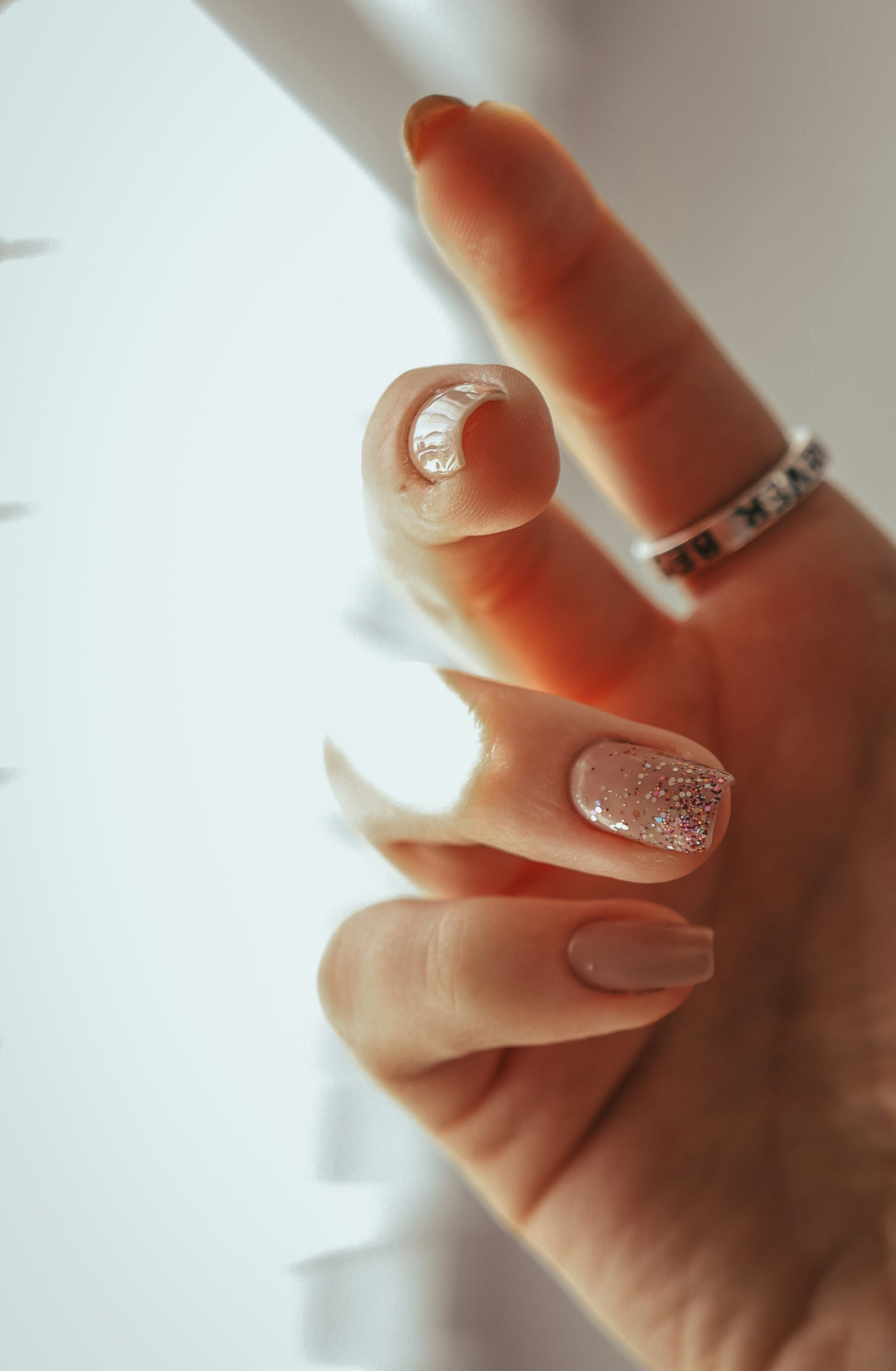 Nude manicure with one glitter accent nail and a ring