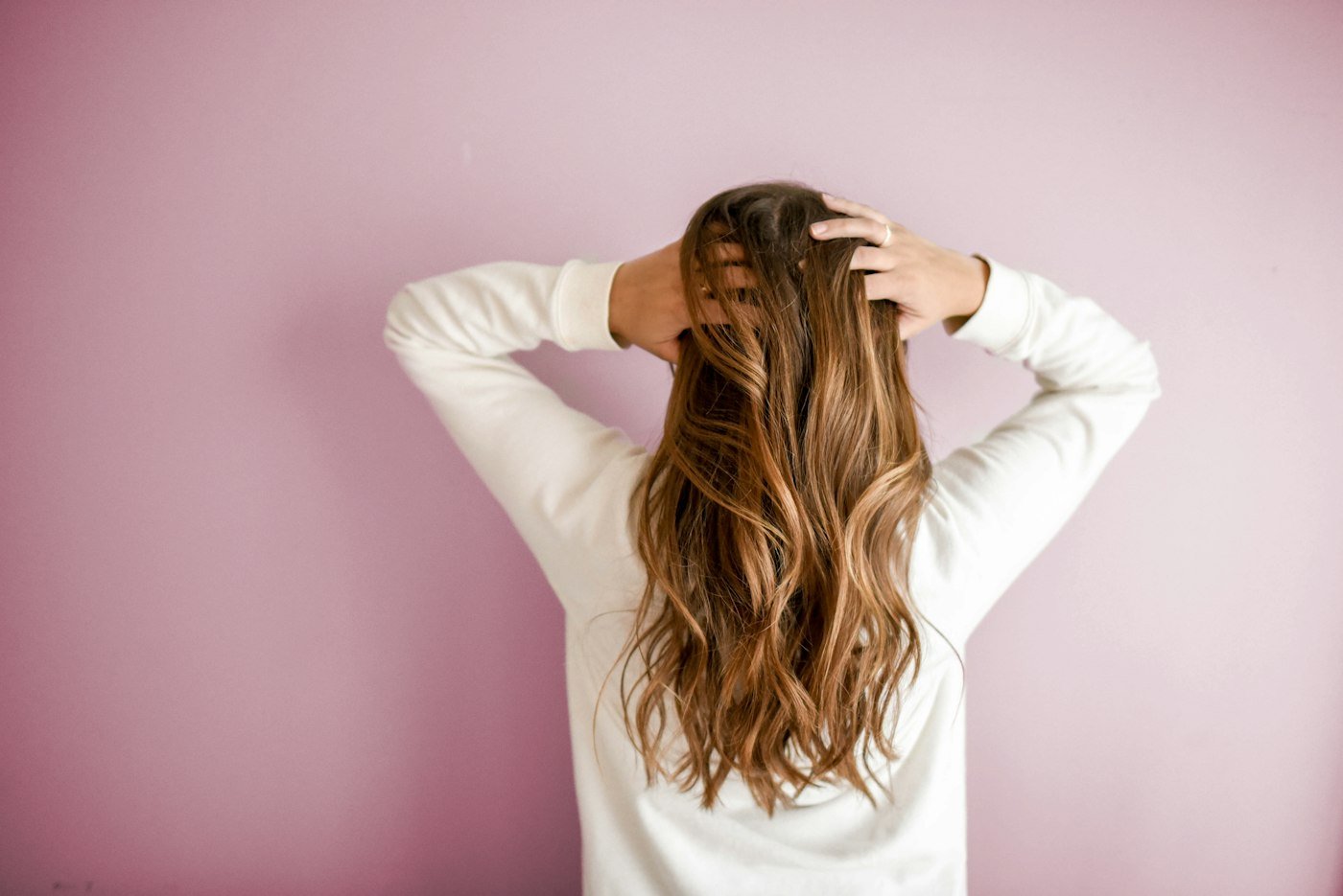 Long glossy brown waves against a pink wall