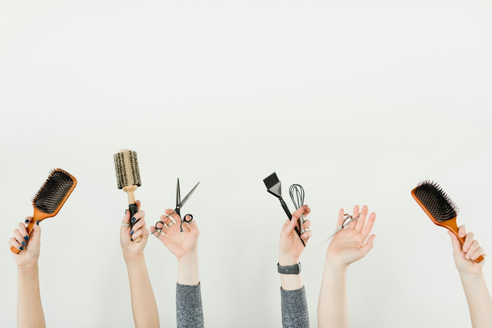 Hands holding hairbrushes, scissors and a tinting brush