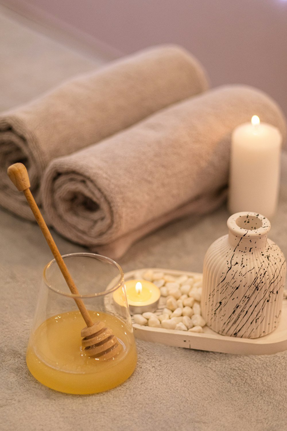 Rolled towels, a candle and honey on a spa tray