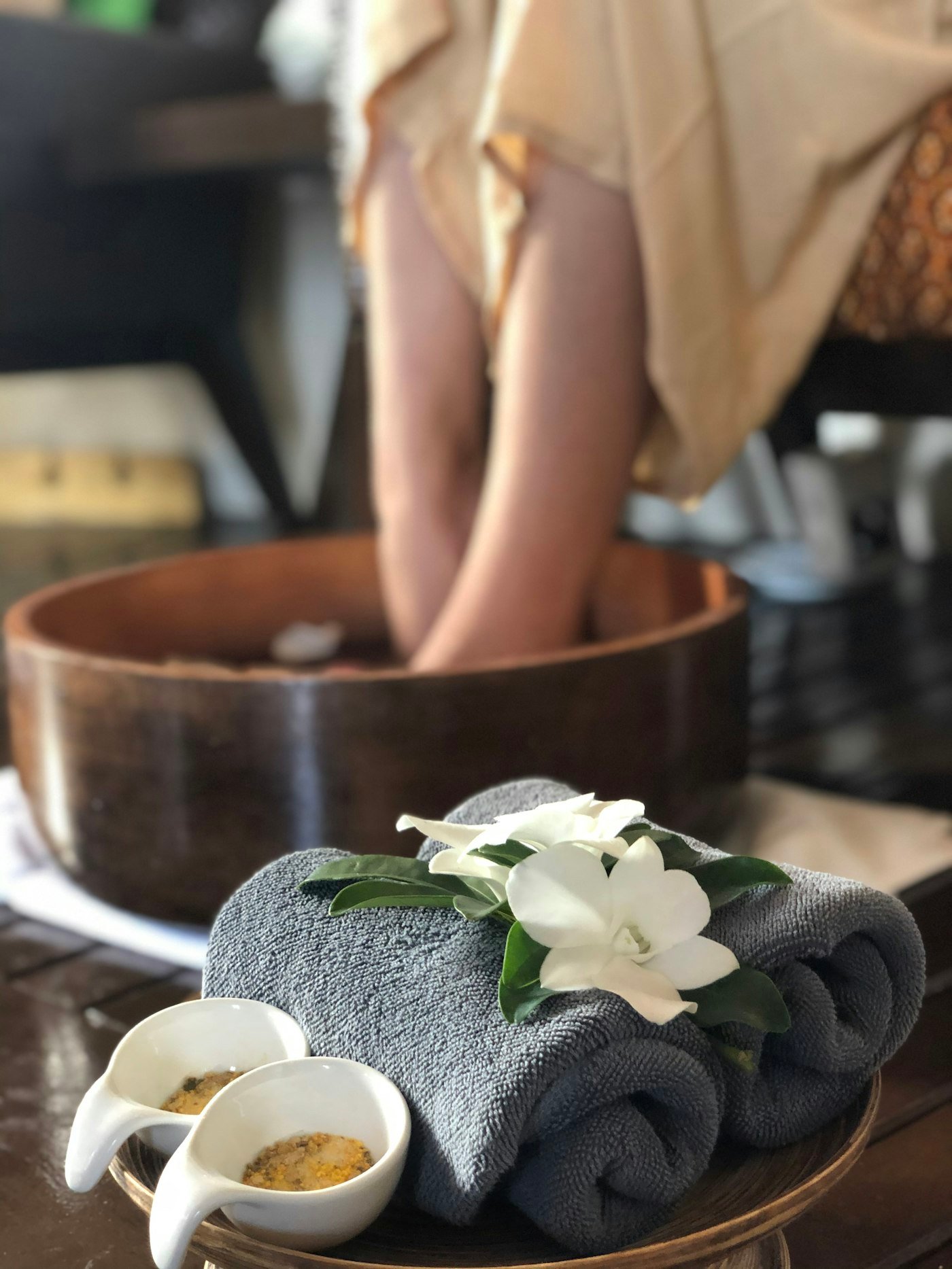 Feet soaking in a warm wooden foot bath with rolled towels and flowers