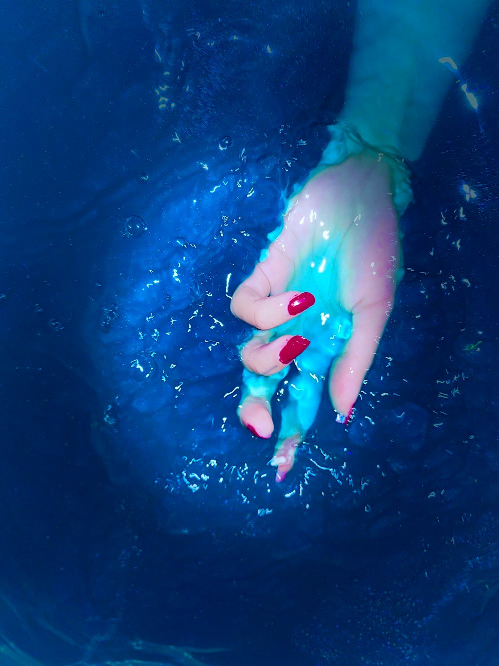 Hand with red nails in clear blue water