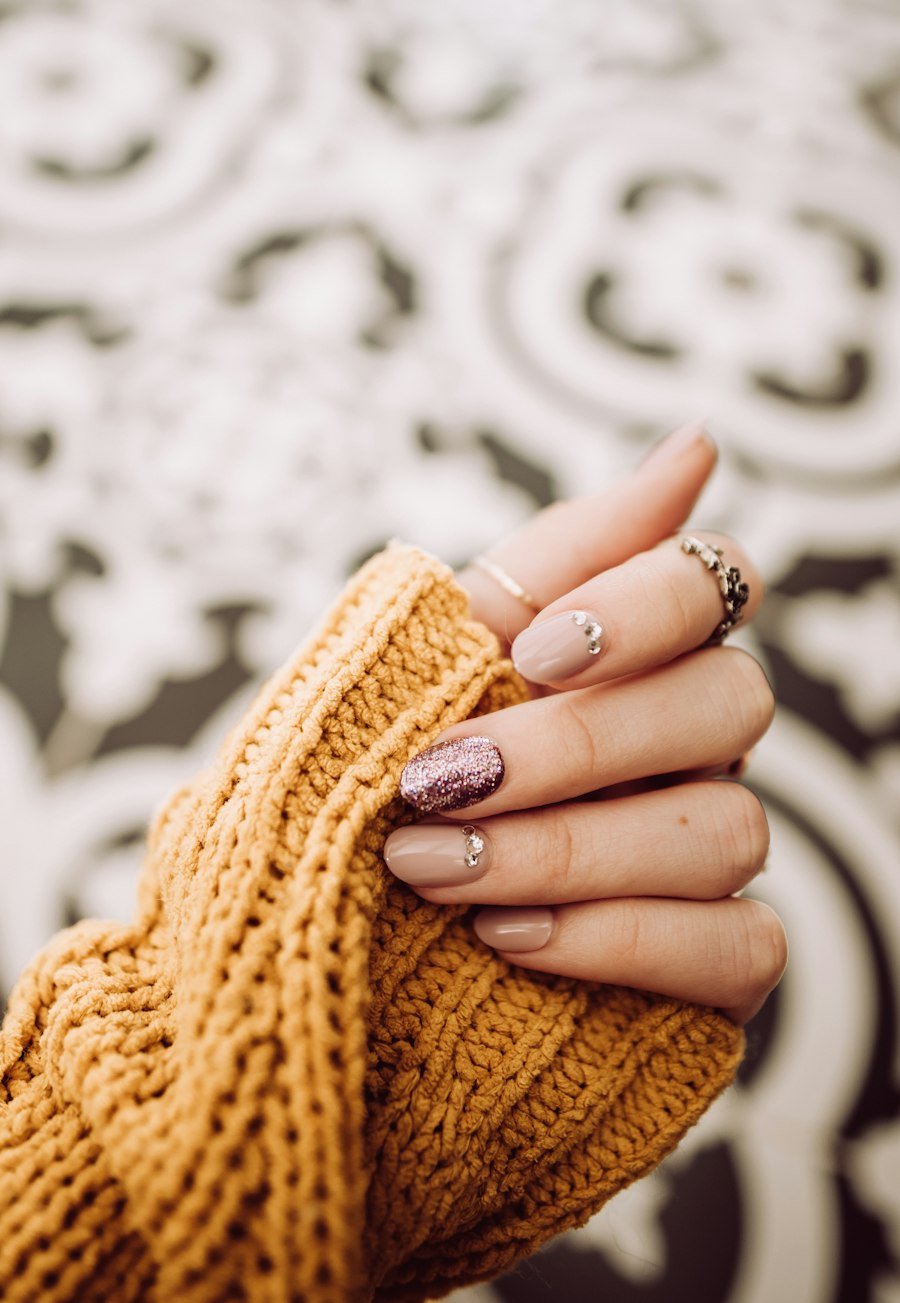 Neutral manicure with rings against a mustard knit